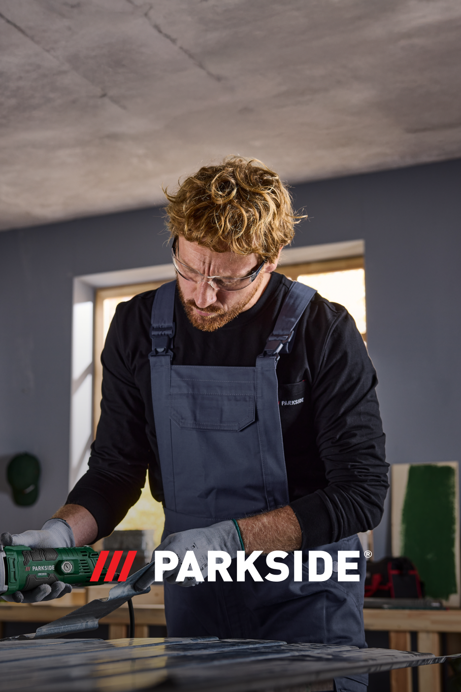 Homem com óculos de proteção e macacão, a usar uma ferramenta elétrica PARKSIDE.