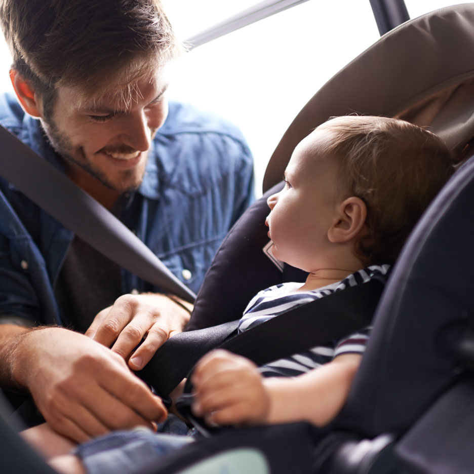 Um pai prende seu bebê na cadeirinha de carro.