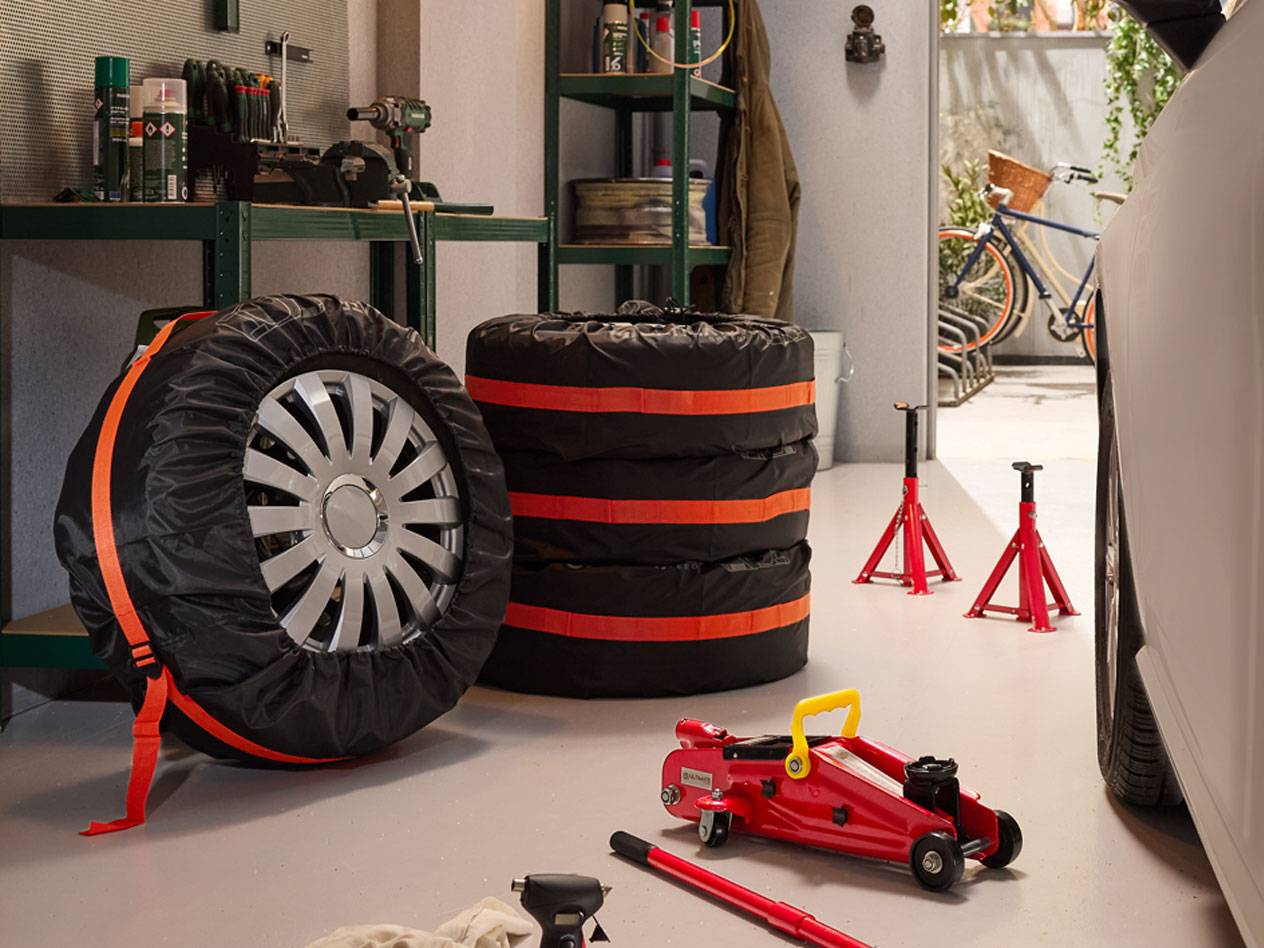 Pneus de inverno embalados com capas, macacos hidráulicos e suportes de carro numa garagem.