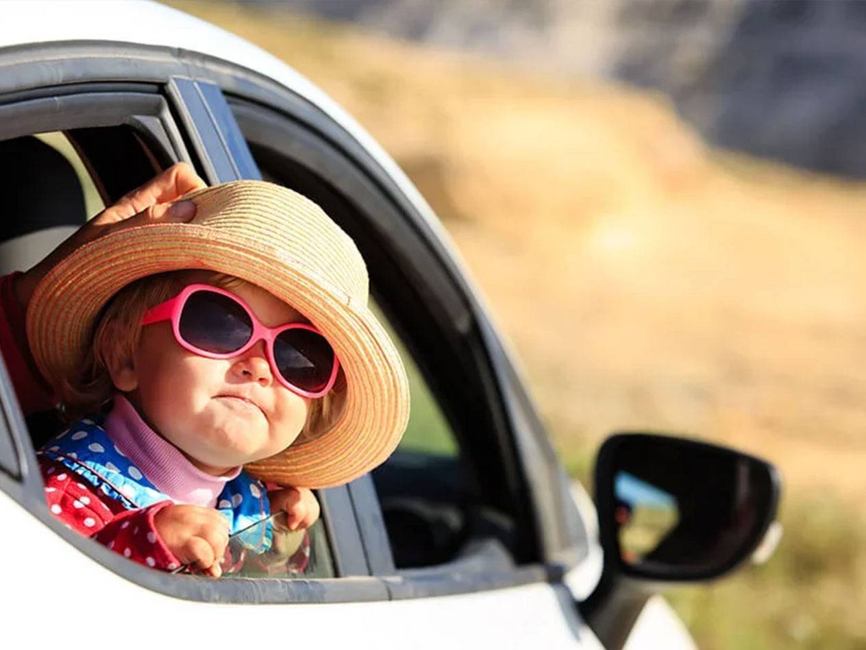 Criança pequena com chapéu e óculos de sol em um carro.