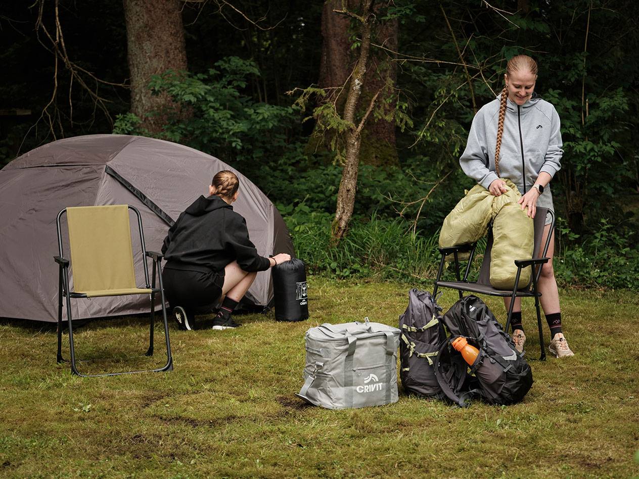 Duas pessoas desempacotam equipamentos de camping, incluindo uma sacola térmica Crivit e uma barraca.