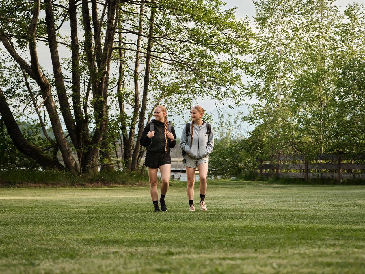 Duas meninas com mochilas caminham em um gramado.