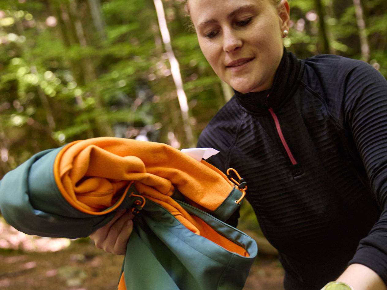 Mulher em uma floresta dobrando uma jaqueta esportiva.