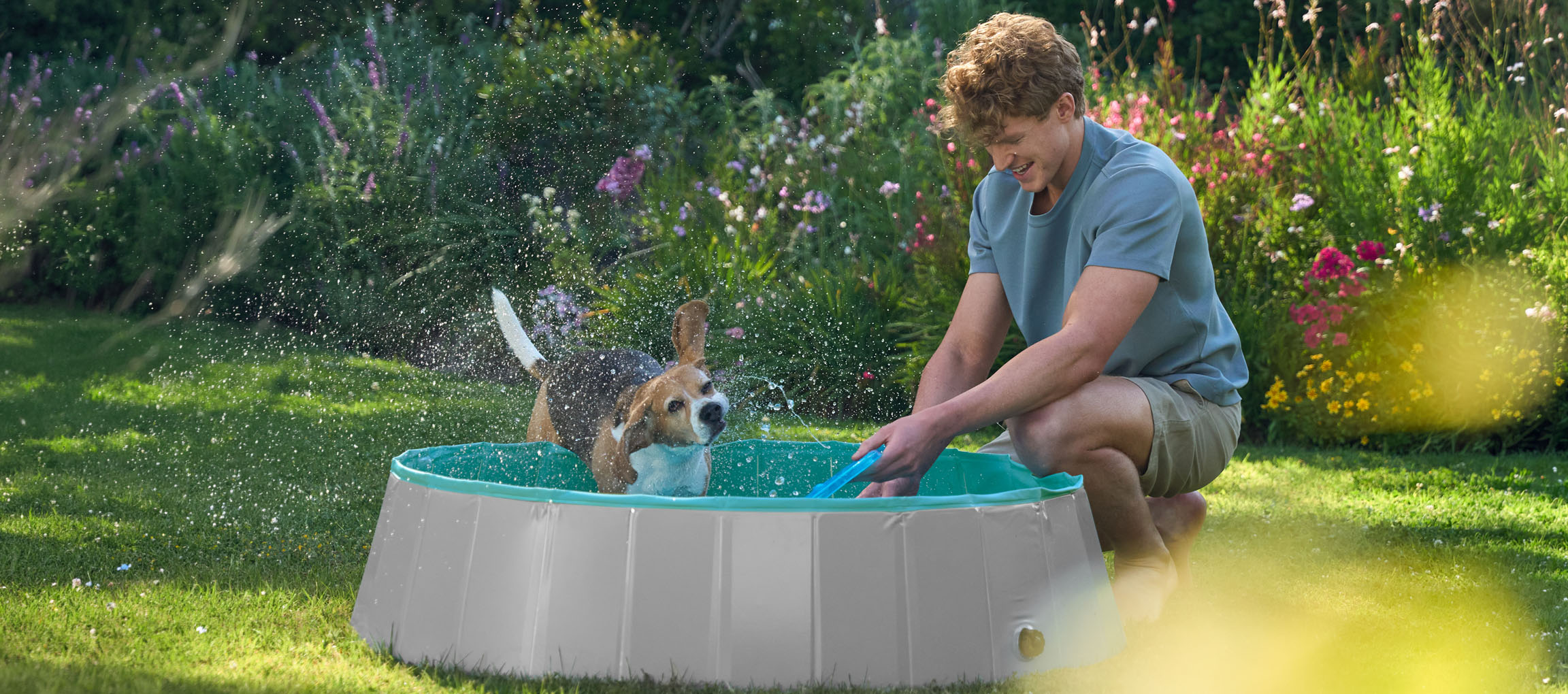 Homem e cão a brincar numa piscina infantil no jardim.