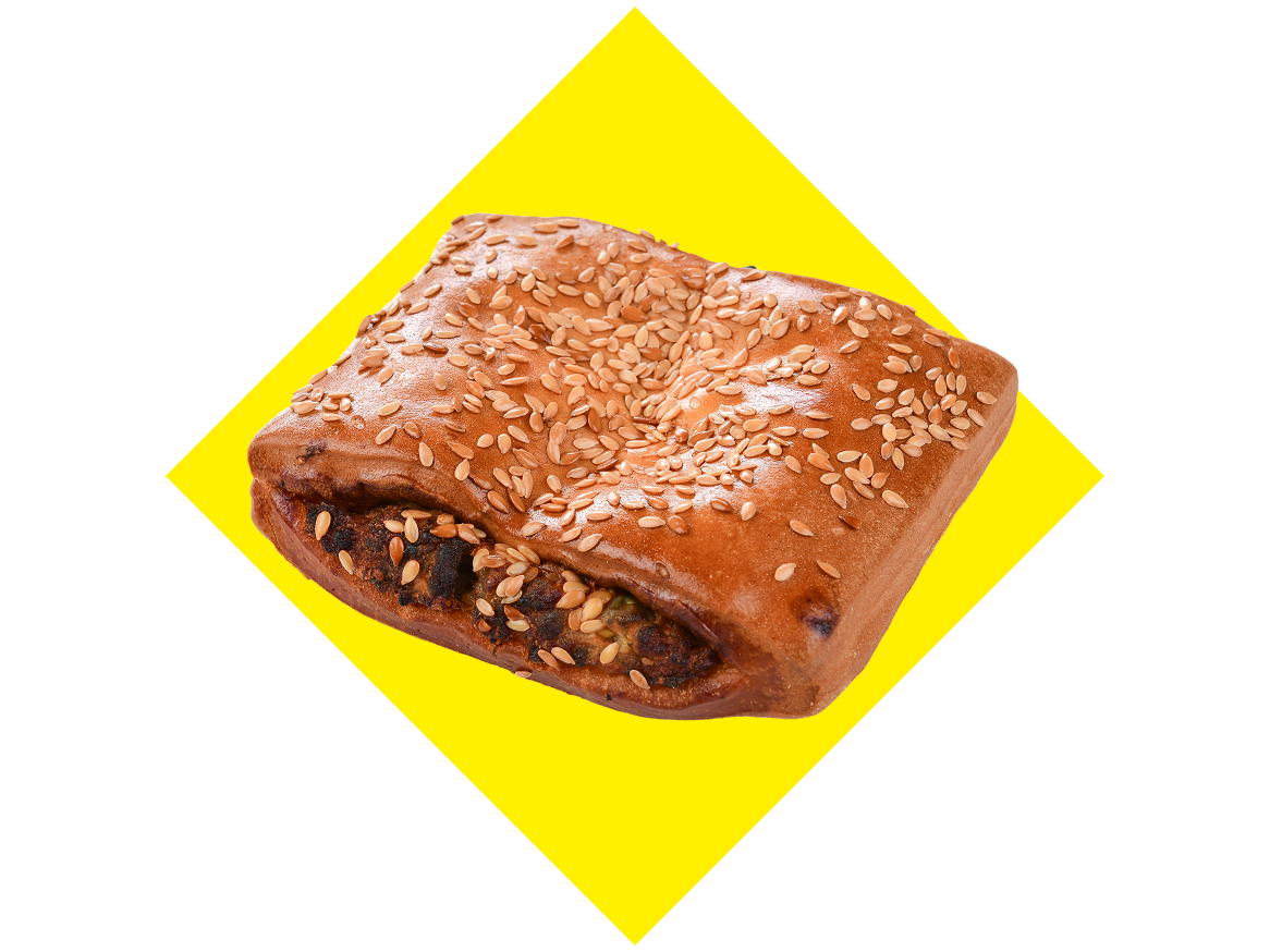 Pão quadrado com sementes de sésamo e recheio salgado, sobre fundo amarelo e preto.